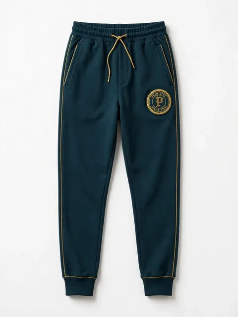 Primitiva pantalon jogger GT en sarcelle et doré avec chevilles à revers et l’emblème sur la cuisse