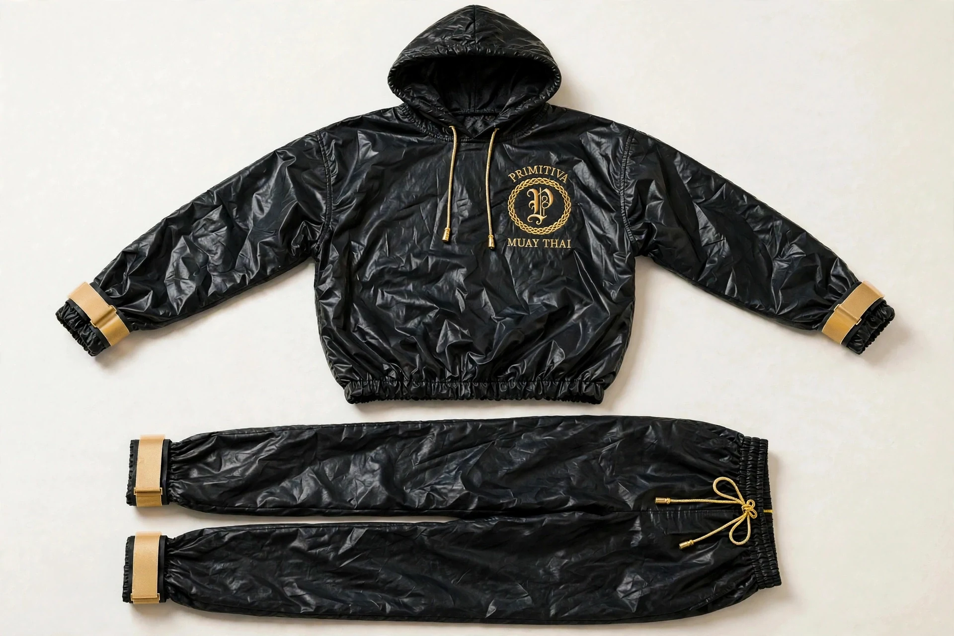 Primitiva Sono BG sauna suit in black and gold — hooded pullover and full-length trousers with sealed strap cuffs and the emblem on the chest